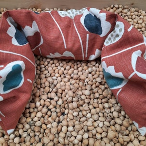 Puede incluir: Una almohada de cuello con estampado floral rojo, blanco y turquesa. La almohada est&aacute; sobre un lecho de semillas de color marr&oacute;n claro.