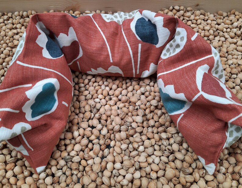 Puede incluir: Una almohada de cuello con estampado floral rojo, blanco y turquesa. La almohada est&aacute; sobre un lecho de semillas de color marr&oacute;n claro.