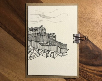 Puede incluir: Un dibujo en blanco y negro de un castillo en un acantilado rocoso. El dibujo está en una tarjeta blanca con un borde marrón.