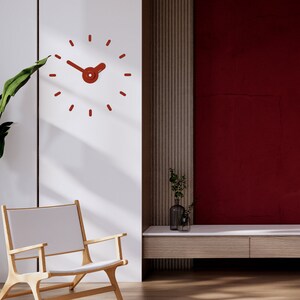 May include: A red clock with a unique design hangs on a white wall in a modern living room. The clock has a simple, minimalist design with a round face and thin hands. The clock is set against a backdrop of a wooden wall panel and a red wall.