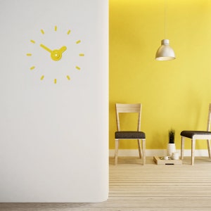 May include: A yellow clock with a simple design hangs on a white wall. Two wooden chairs with black seats face a yellow wall with a hanging light fixture. A small wooden table with two white ceramic cups and a potted plant sits in front of the chairs.