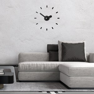 May include: A gray sectional sofa with black pillows in a living room setting. A black clock with a simple design is on the wall.