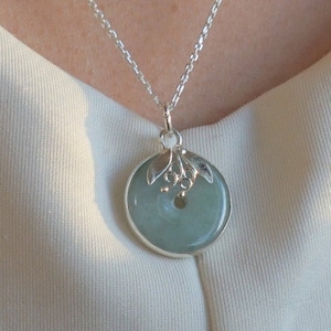 May include: A silver chain necklace with a round jade pendant. The pendant has a silver floral design.