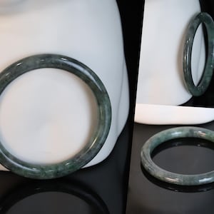 May include: A green jade bangle bracelet. The bracelet is smooth and polished, with a dark green color.