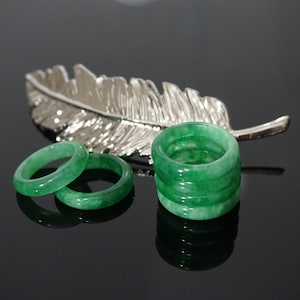 May include: A set of five green jade rings stacked on top of each other. Two additional green jade rings are lying next to the stack.