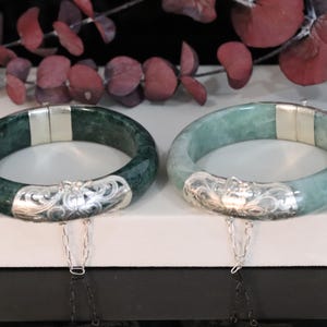 Könnte beinhalten: Zwei Jade-Armbänder mit silbernen Akzenten. Die Armbänder sind grün und hellgrün und haben ein florales Design auf den silbernen Akzenten.