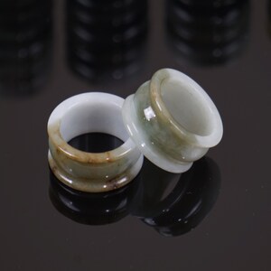 May include: Two jade rings with a green and brown colour scheme. The rings are stacked on top of each other.