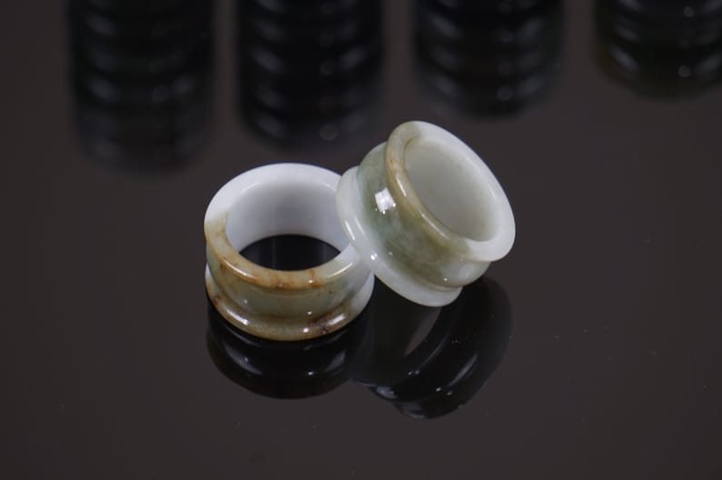 May include: Two jade rings with a green and brown colour scheme. The rings are stacked on top of each other.