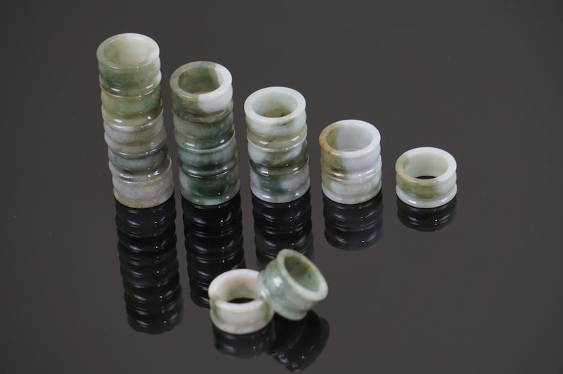May include: A set of jade rings stacked in decreasing size, with the largest stack being 10 rings high. The rings are a mottled green and white colour.