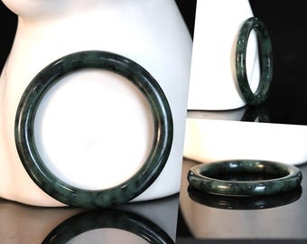 May include: A dark green jade bangle bracelet. The bracelet is smooth and polished, with a subtle marbled pattern.