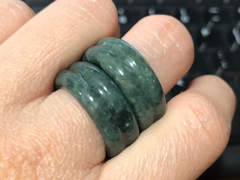 May include: Two jade green rings stacked on a finger. The rings are smooth and have a slightly rounded shape.
