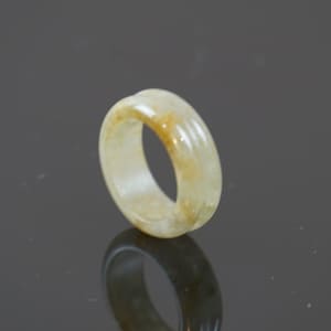 May include: A pale yellow jade ring with a smooth, polished surface. The ring has a simple, elegant design and is a beautiful example of jade craftsmanship.