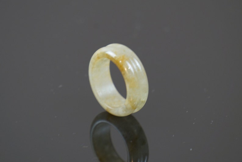 May include: A pale yellow jade ring with a smooth, polished surface. The ring has a simple, elegant design and is a beautiful example of jade craftsmanship.