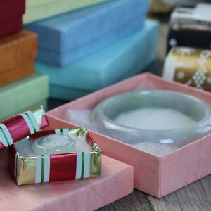 May include: Two small gift boxes with lids open. The box on the left is red, white and green with a white interior. The box on the right is pink with a white interior and a light green bowl inside.