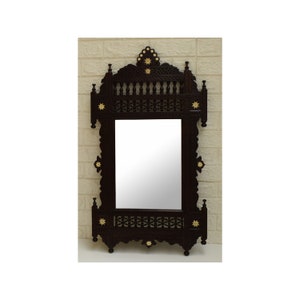 May include: A dark brown wooden mirror with intricate carvings and gold accents. The mirror has a rectangular shape with a decorative top and bottom.