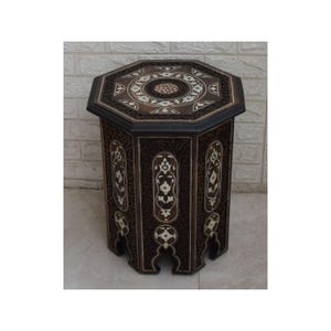 Könnte beinhalten: Achteckiger Holztisch mit aufwendigen Schnitzereien und eingelegten Perlmuttdetails. Der Tisch hat eine dunkelbraune Oberfläche und ein geometrisches Design.