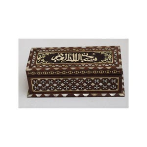 Op de afbeelding: Een rechthoekige houten doos met ingewikkelde inlegwerk van parelmoer en goud. De bovenkant van de doos heeft de Arabische zin "Subhanallah" in gouden letters.