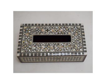 May include: Rectangular tissue box with a decorative mother-of-pearl inlay. The box features a geometric pattern with black, white, and iridescent accents. The central opening is a dark rectangle.