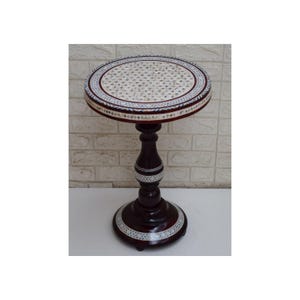 Op de afbeelding: Een ronde, houten bijzettafel met een donkerbruine basis en een wit en blauw ingelegd blad. De tafel heeft een sokkel met een decoratief ontwerp.