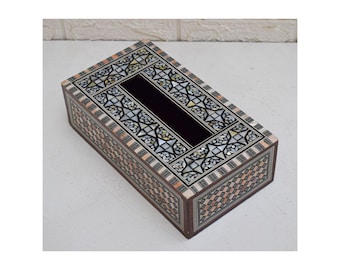 May include: Rectangular wooden tissue box with intricate inlaid mother-of-pearl and geometric patterns. The box features a dark, rectangular opening for tissue dispensing. The sides and top are adorned with detailed mosaic designs in various colors.