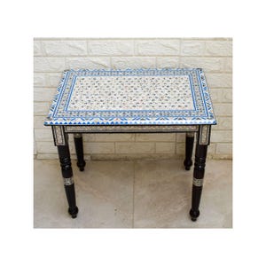 May include: A rectangular side table with a white surface adorned with a speckled pattern and a blue border. The table has four dark brown legs with silver accents. The table is approximately 24 inches long, 18 inches wide, and 20 inches tall.