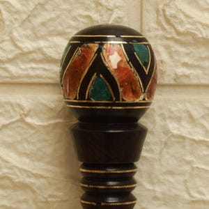 Puede incluir: Un tap&oacute;n de botella decorativo negro con una parte superior redonda con piedras de colores incrustadas y detalles dorados. El tap&oacute;n tiene una base de madera oscura con un dise&ntilde;o detallado. El dise&ntilde;o general es ornamentado y elegante.