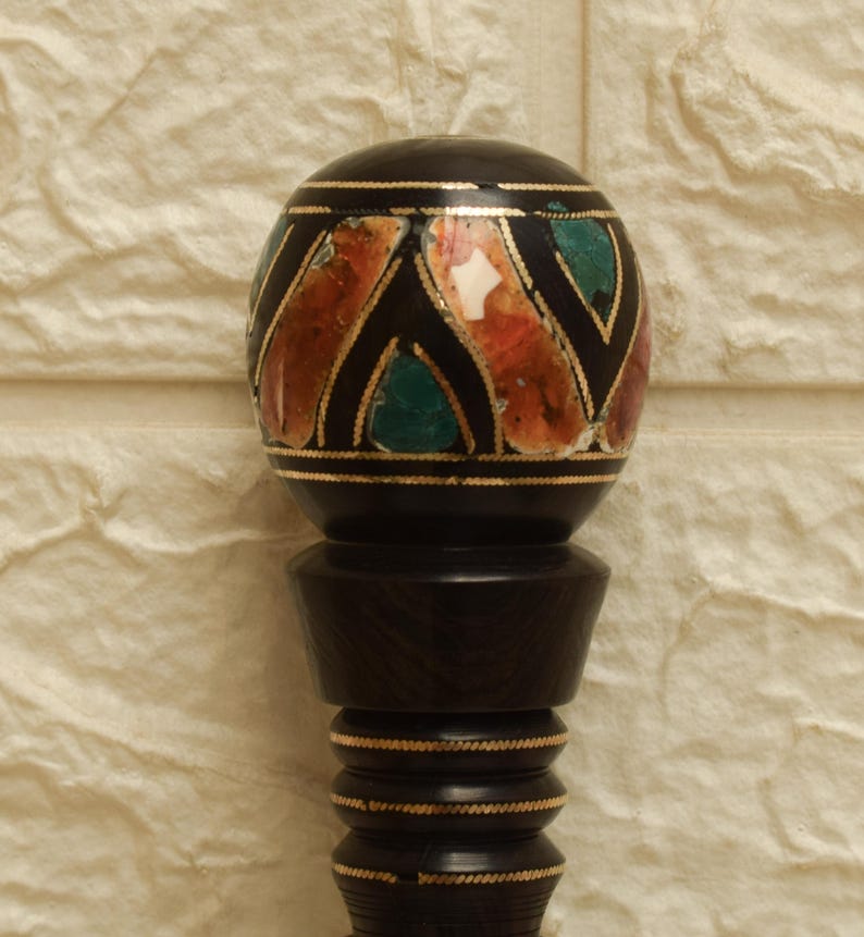 Puede incluir: Un tap&oacute;n de botella decorativo negro con una parte superior redonda con piedras de colores incrustadas y detalles dorados. El tap&oacute;n tiene una base de madera oscura con un dise&ntilde;o detallado. El dise&ntilde;o general es ornamentado y elegante.