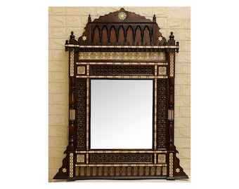 Puede incluir: Un espejo de madera grande y ornamentado con tallas e incrustaciones intrincadas. El marco es de color marrón oscuro con detalles de marfil. El espejo tiene una forma rectangular con un arco puntiagudo en la parte superior.