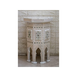 Könnte beinhalten: Ein weißer achteckiger Beistelltisch mit aufwendigen Schnitzereien und eingelegten Perlmuttdetails. Der Tisch hat ein geometrisches Design und vier Beine.