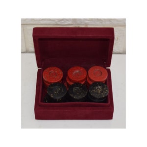 May include: A set of red and black checkers in a burgundy velvet lined box. The checkers are made of a speckled material.