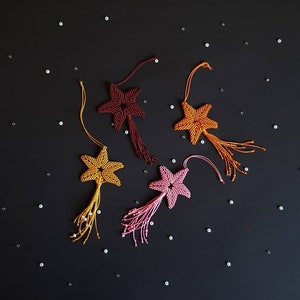 May include: Four handmade macrame star ornaments with tassels. The stars are in shades of orange, yellow, and pink. The tassels are made of beads.