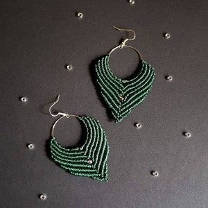 Könnte beinhalten: Ein Paar grüne Makramee-Ohrringe in Tropfenform. Die Ohrringe sind aus dunkelgrünem Garn gefertigt und haben einen silbernen Ring.