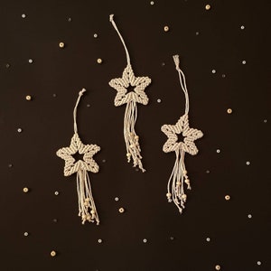 May include: Three white macrame star ornaments with wooden beads hanging from a dark background.