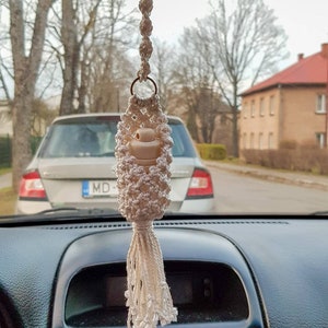 Könnte beinhalten: Ein weißer gehäkelter Auto-Lufterfrischer mit einem Quasten, der am Rückspiegel eines Autos hängt. Der Lufterfrischer hat einen kleinen weißen Keramikdiffusor im Inneren.
