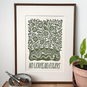 Puede incluir: Una impresión artística enmarcada con temática botánica. La impresión presenta un diseño floral verde y blanco con el texto "NO WORMS, NO FLOWERS". La obra de arte se muestra en un marco de madera marrón, con un passe-partout blanco.