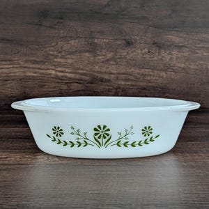 May include: White oval casserole dish with green floral design. The dish has a slightly flared rim and is decorated with stylized green flowers and leaves. The dish is made of a durable material and is suitable for baking and serving.