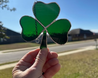 May include: A green stained glass shamrock with a silver chain hanging from the top.