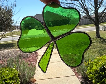 May include: A green stained glass shamrock with a silver chain hanging from the top. The shamrock is a popular symbol of Ireland and good luck.