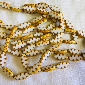 May include: A strand of white and brown ceramic beads with a wavy pattern. The beads are oval shaped and have a glossy finish.