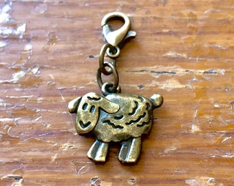 May include: A bronze-colored sheep charm with a lobster clasp. The sheep has a smiling face and detailed wool texture. The charm is attached to a small chain and is suitable for jewelry making or as a decorative accent.