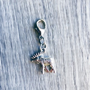 May include: A silver-colored charm featuring a detailed moose pendant. The charm has a lobster clasp for easy attachment to a bracelet or necklace. The moose has detailed antlers and a textured body.