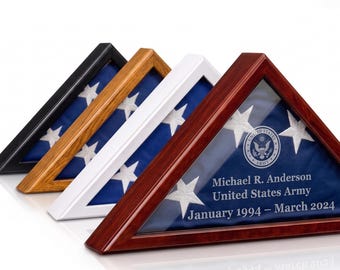 May include: Four triangular flag display cases in black, oak, white, and cherry wood finishes. Each case holds a folded American flag. The cherry case features engraved text: Michael R. Anderson, United States Army, January 1994 – March 2024.