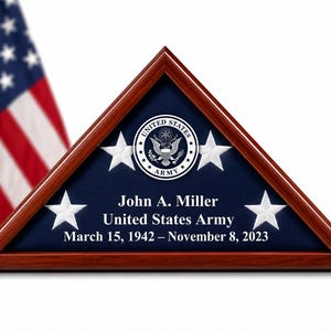 May include: A triangular wooden display case with a dark cherry finish containing a blue velvet backing. The case features the United States Army seal, four embroidered white stars, and the text John A. Miller, United States Army, March 15, 1942 – November 8, 2023.