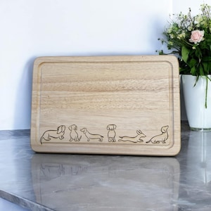 May include: A wooden cutting board with a design of seven dachshunds in various poses. The board is light brown and has a slightly raised edge.