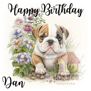 May include: Happy Birthday Dan! A cute white and brown bulldog puppy sits in a bed of pink and purple flowers.