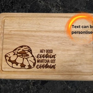 May include: A wooden cutting board with a snake design and the text "Hey good lookin' Whatcha got cookin'". The text can be personalised.
