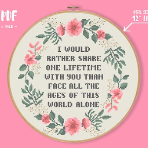 Peut inclure: Un motif de point de croix avec une couronne de fleurs composée de fleurs roses et de feuilles vertes entourant le texte "Je préférerais partager une vie avec toi plutôt que de faire face à tous les âges de ce monde seule". Le motif est conçu pour un cercle de 30 cm.
