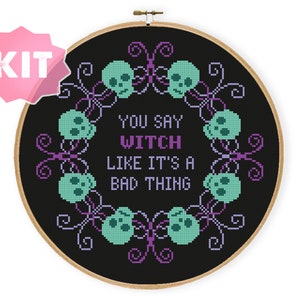 May include: Cross-stitch kit featuring a black background with the text "YOU SAY WITCH LIKE IT'S A BAD THING." The design includes teal skulls and purple decorative elements, all within a wooden embroidery hoop. A pink "KIT" label is in the upper left corner.