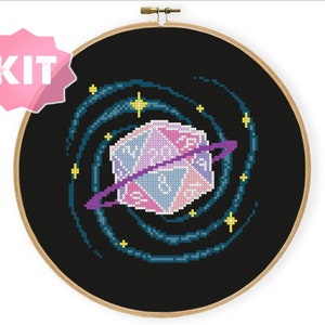 Può includere: Un kit di punto croce con un dado viola e rosa con un vortice di stelle blu e gialle intorno, che rappresenta una galassia.