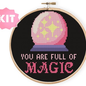 May include: A pink and purple cross-stitch embroidery kit with a black background. The design features a pink magic eight ball with yellow stars inside and the text "YOU ARE FULL OF MAGIC".